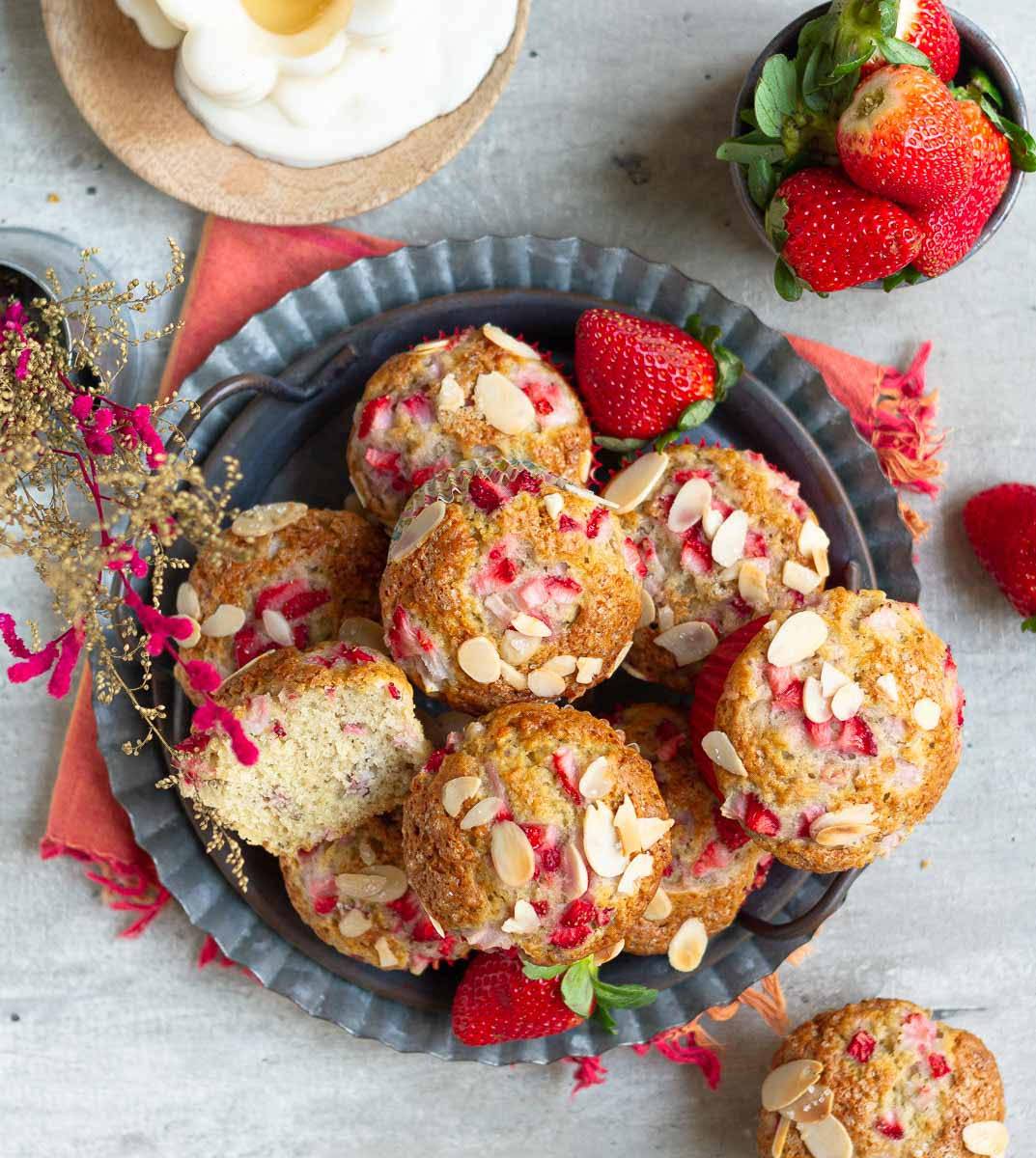 Muffins with strawberries and almonds on a gray tray.