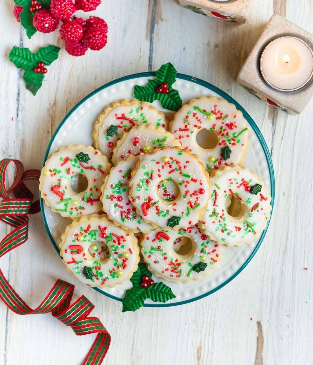 Decorated wreath cookies on a plate with Christmas decorations around.