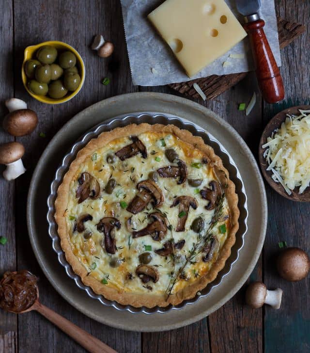 Mushroom quiche on a plate with ingredients around.