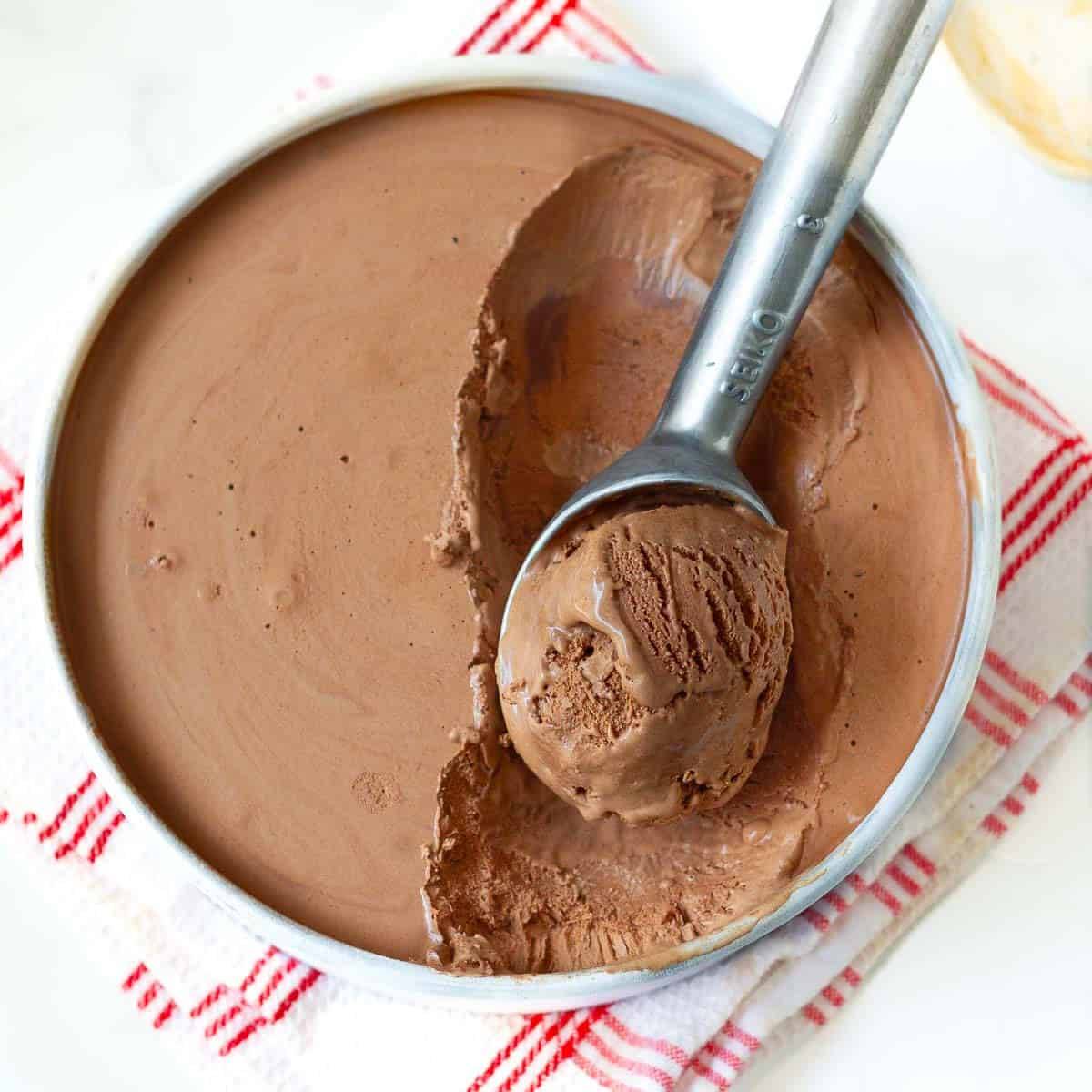 Chocolate ice cream in a round pan with one scoop taken out in an ice cream scoop.