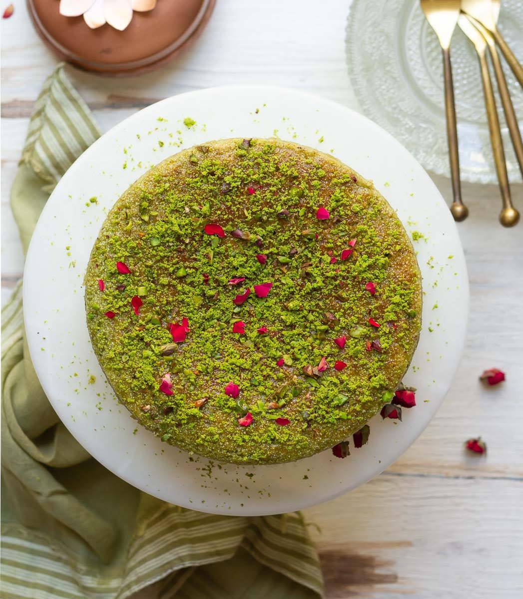 Pistachio cake with chopped pistachios and rose petals on a cake stand.