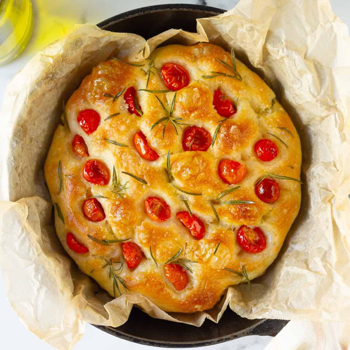 Focaccia with cherry tomatoes in a parchment-lined skillet.