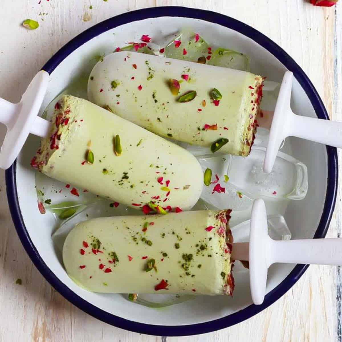 3 matcha popsicles in a white bowl with ice.