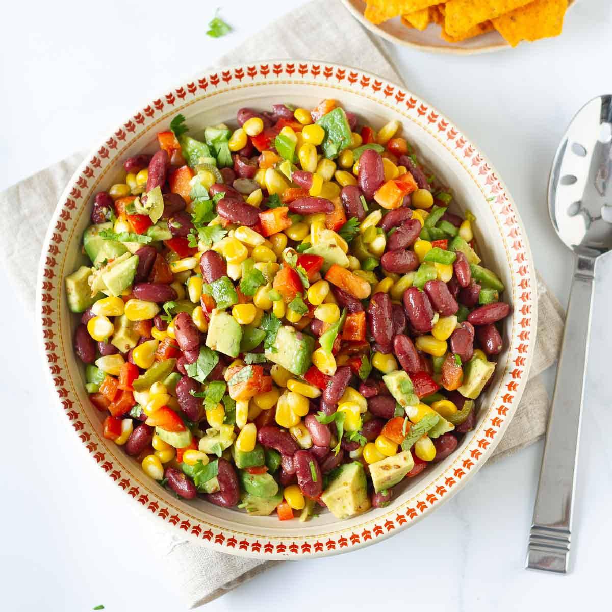 A bowl of corn bean avocado salad with a spoon on the side.