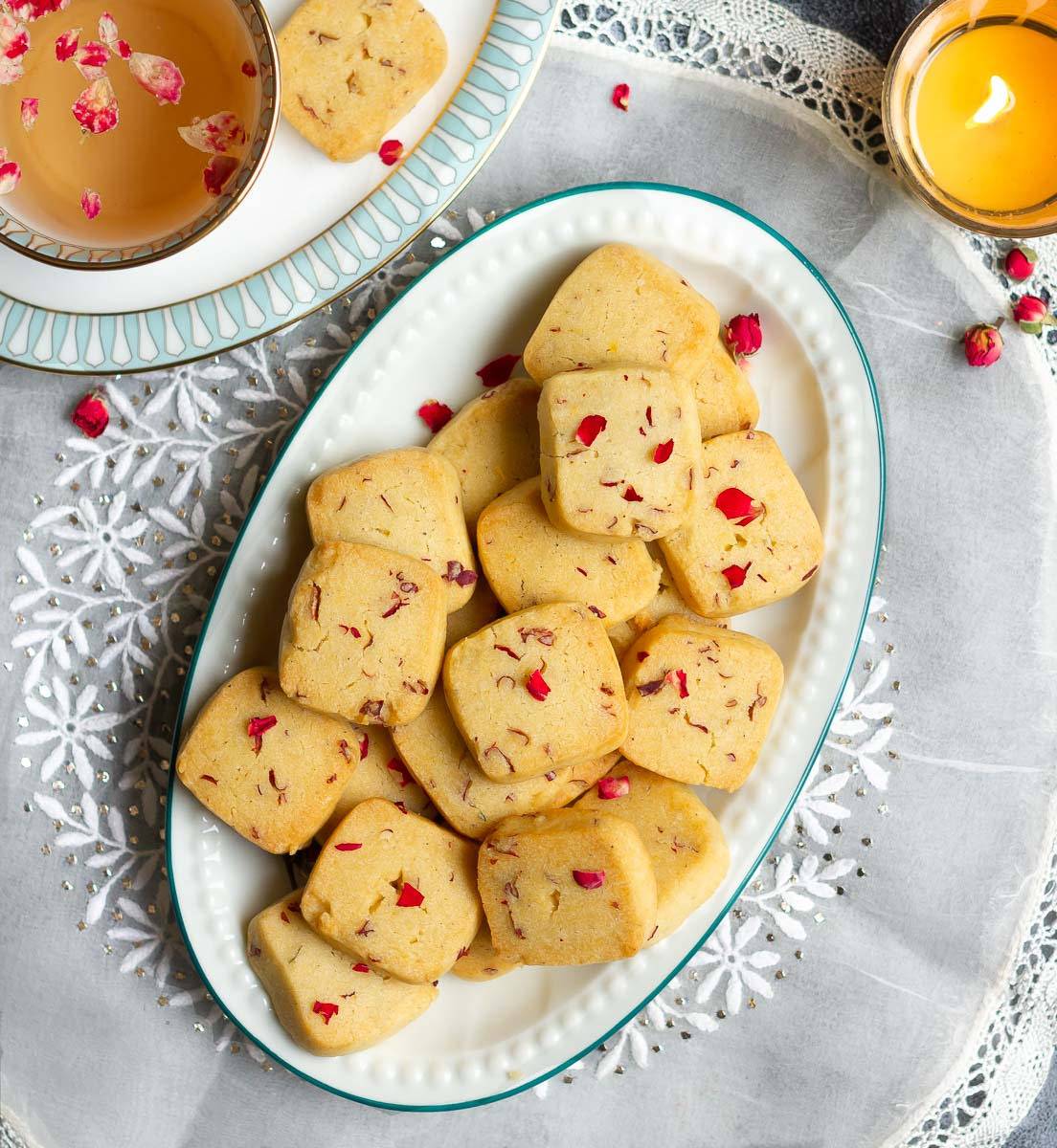 A platter with rose shortbread cookies and a cup of tea on the side.