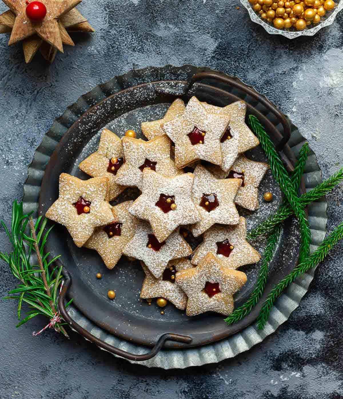 A grey metal tray with Linzer cookies and Christmas greens around.