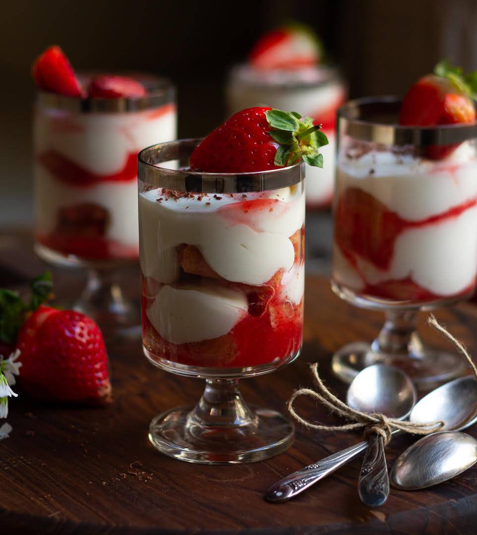 4 glasses filled with strawberry tiramisu with spoons on the side.