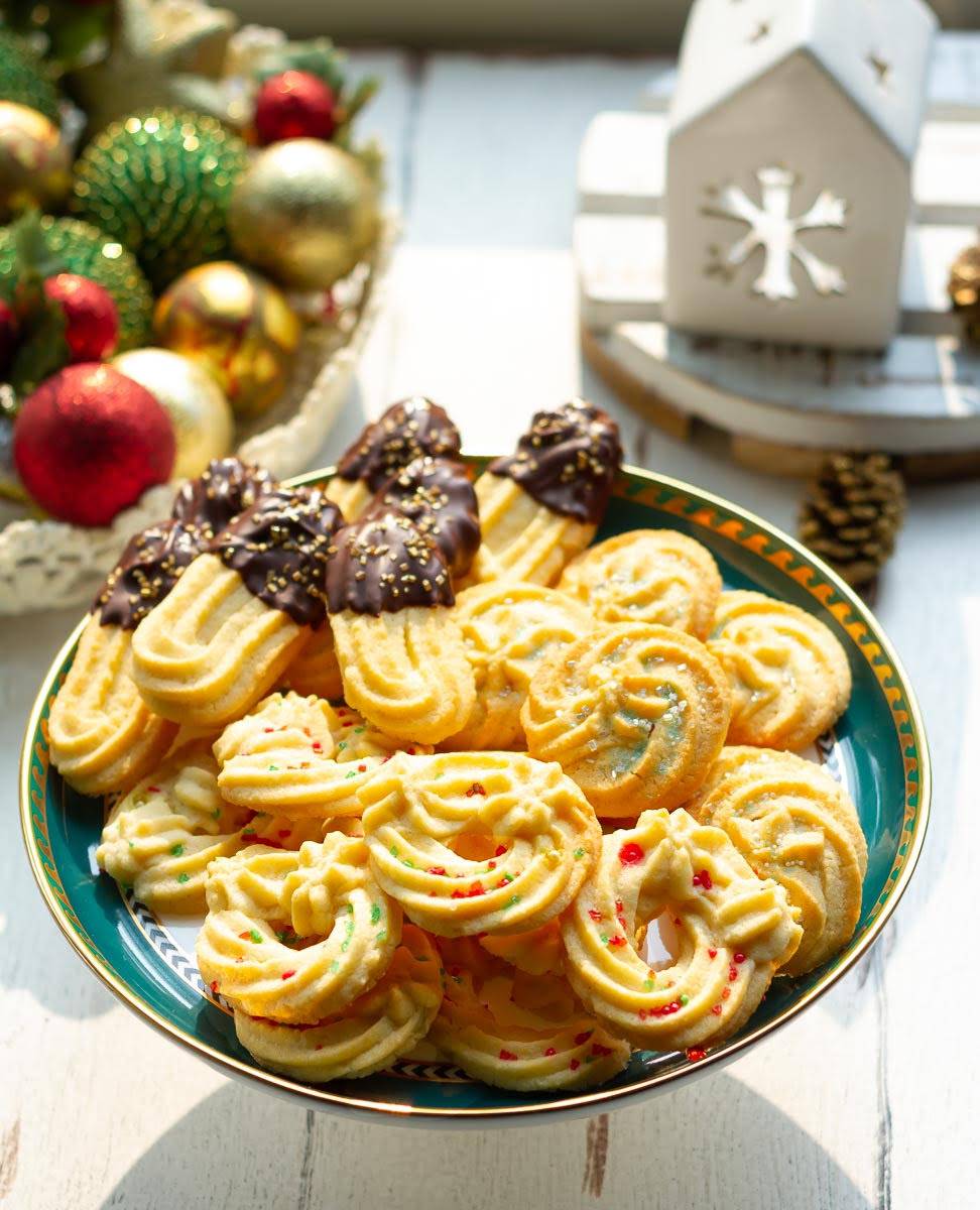 Decorated Spritz cookies on a cake stand with Christmas decorations around.