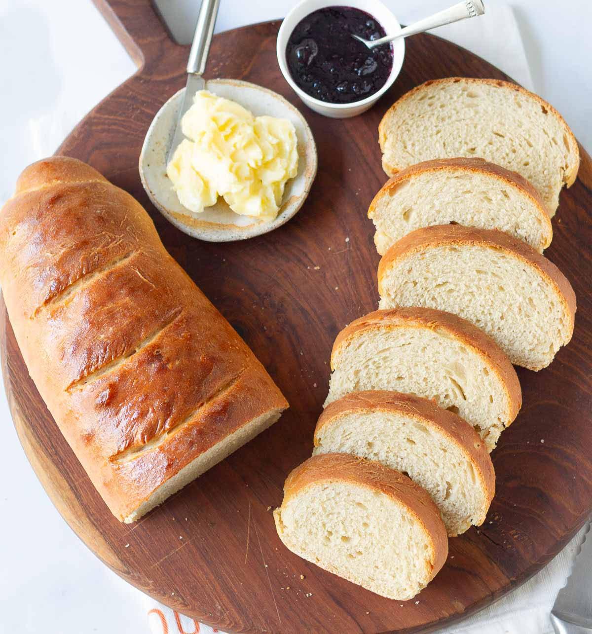 Half a loaf of bread and sliced bread on a wooden board with butter and jam.