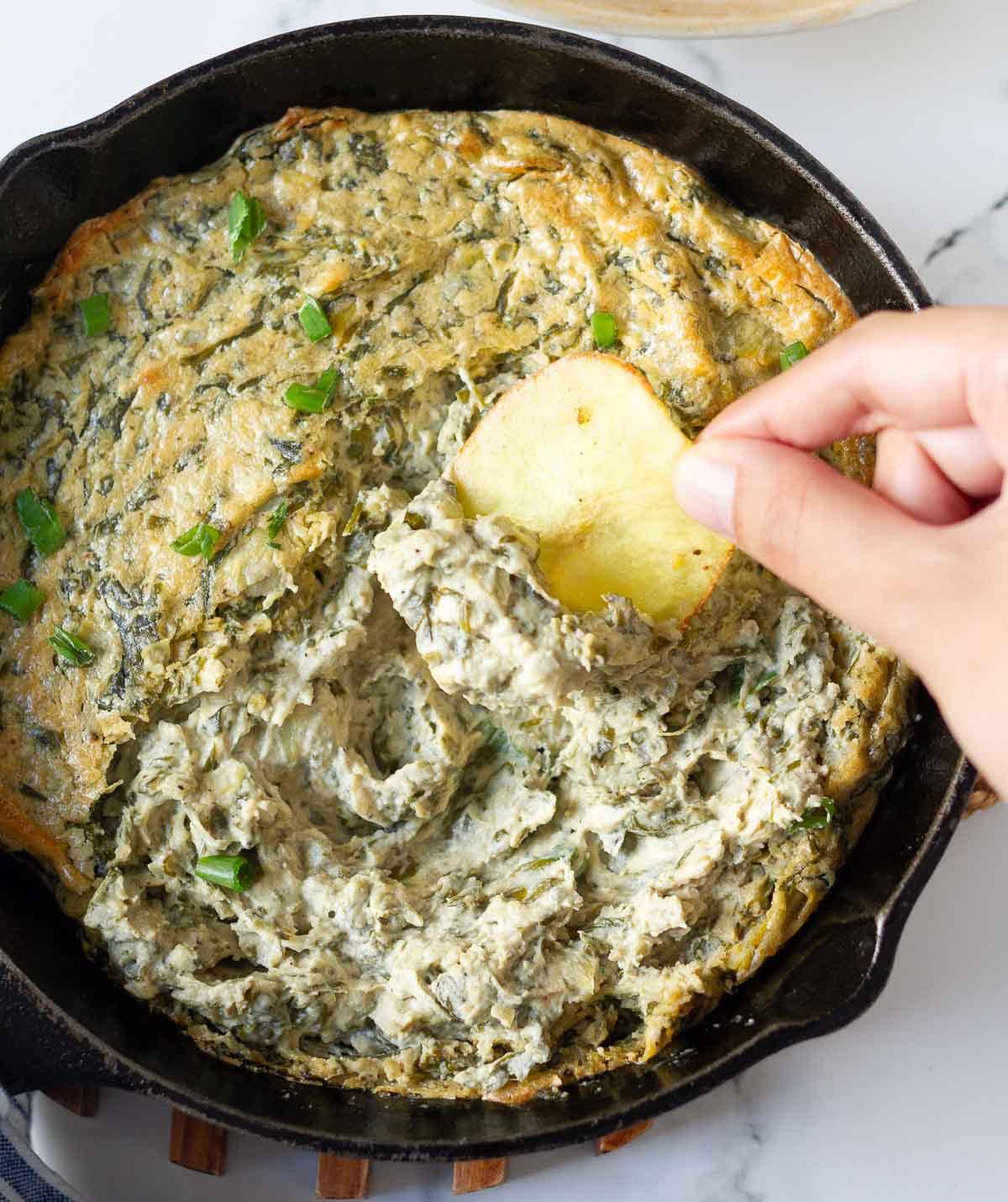A hand scooping out dip with a potato chip.