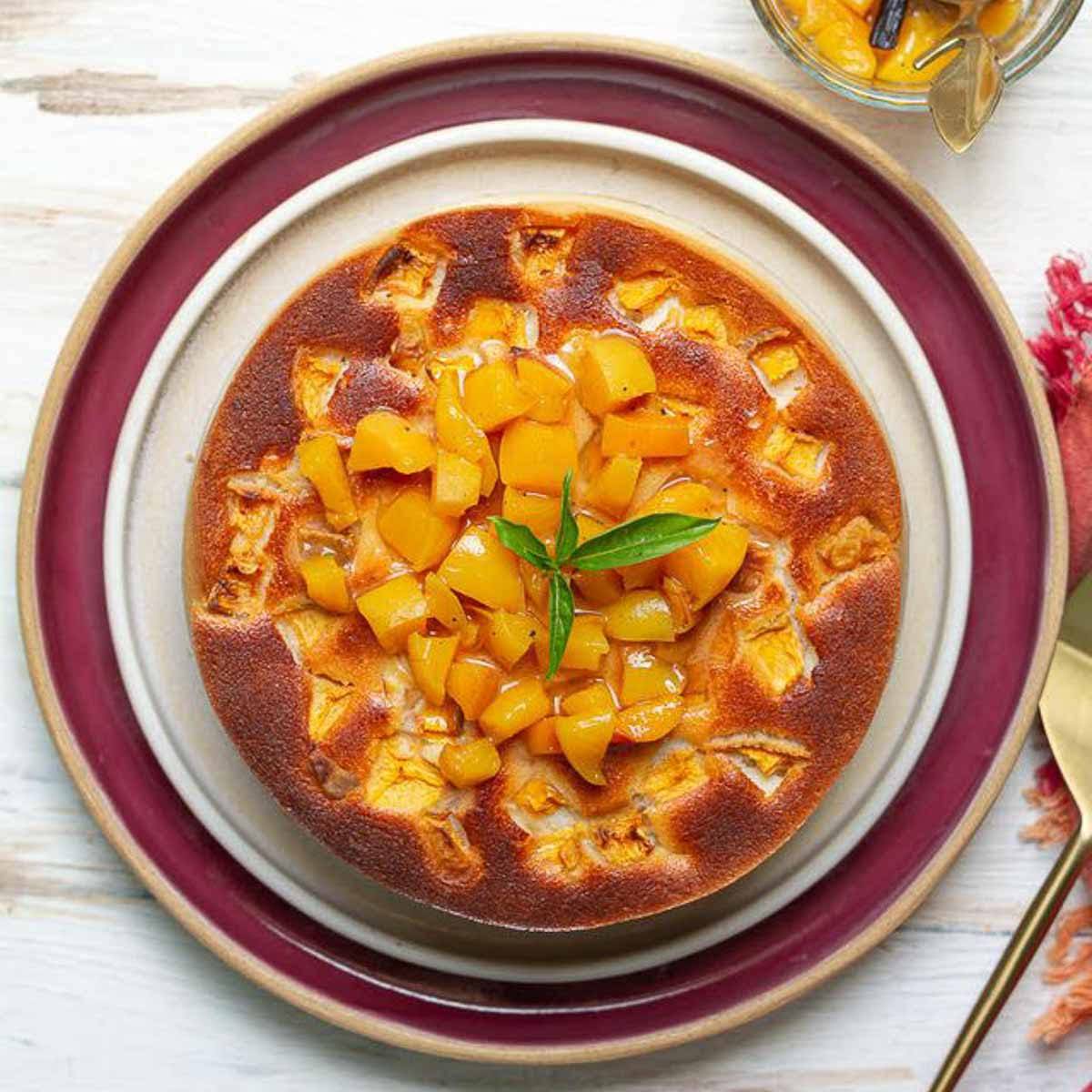 A peach cheesecake with peaches and mint on top on a plate.