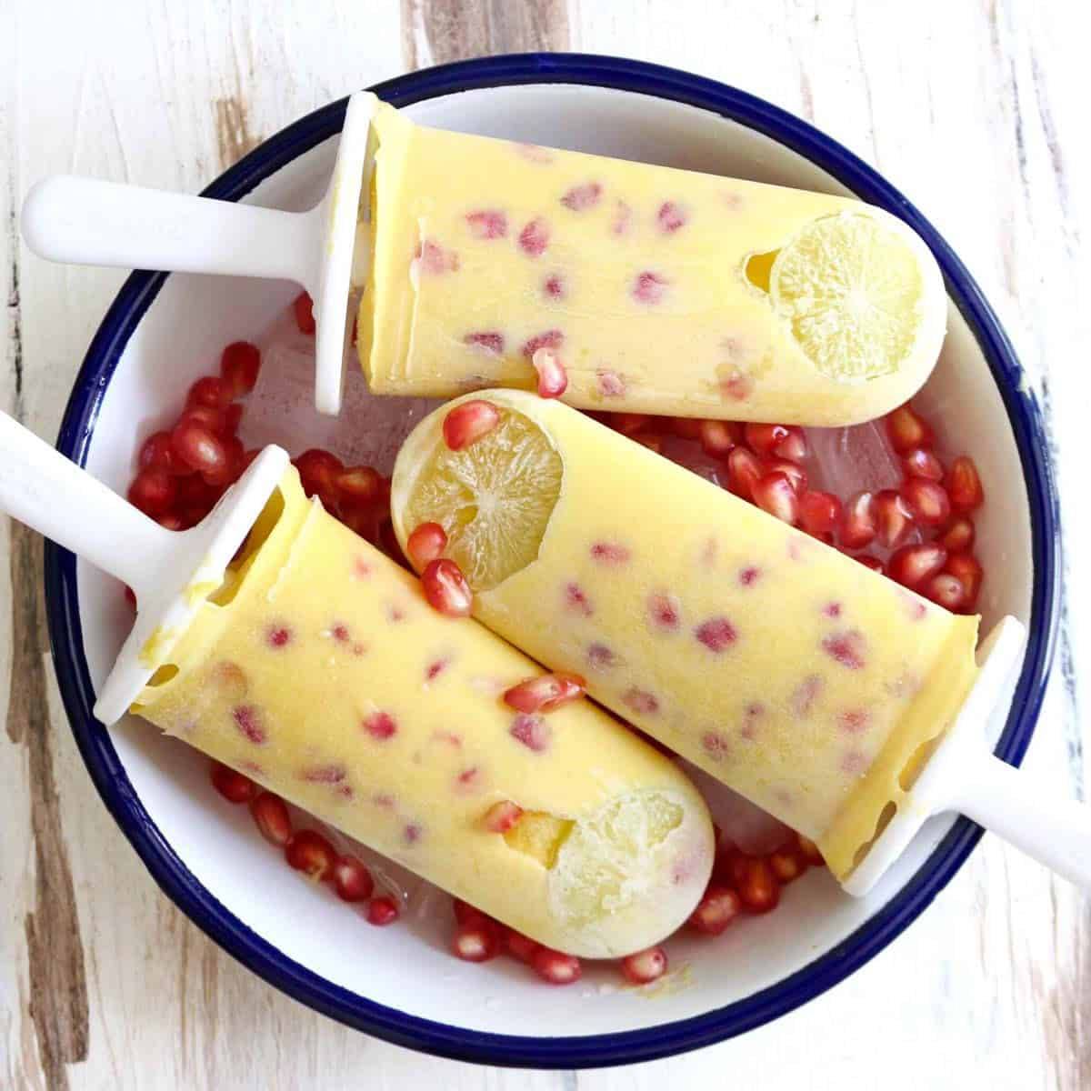 3 mango popsicles in a bowl with pomegranates.