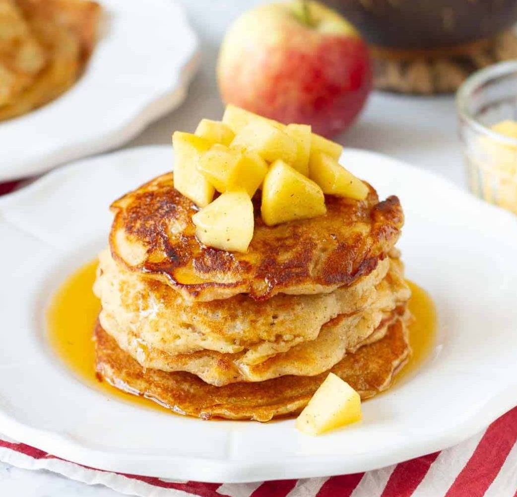 A stack of pancakes with apples and maple syrup on top.