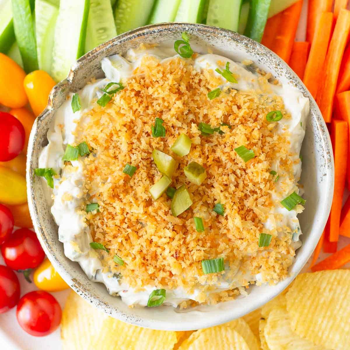 A dip in a bowl with veggies and chips around.