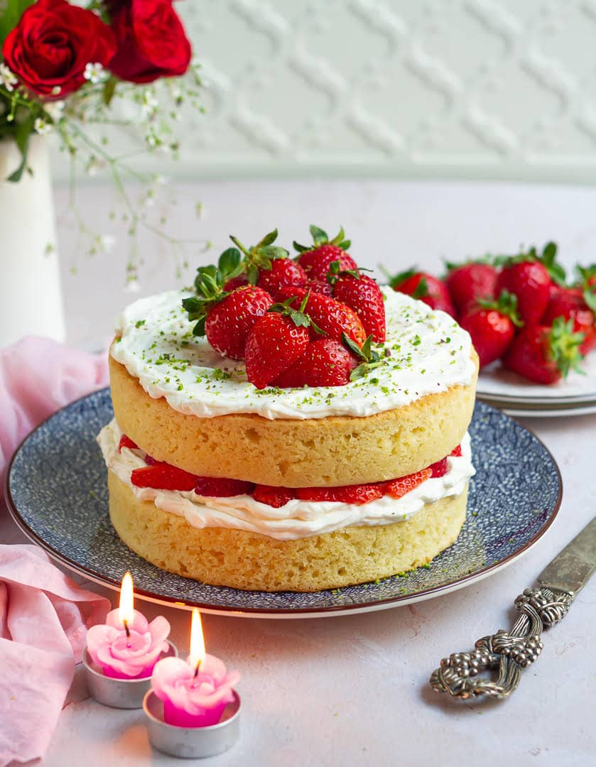A layer cake with strawberries and cream on a blue platter.