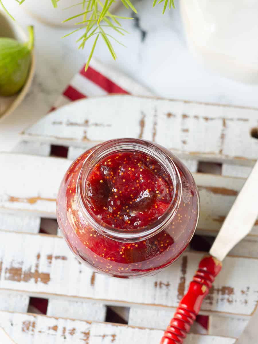 A jar of fig jam on a trivet with a knife on the side.