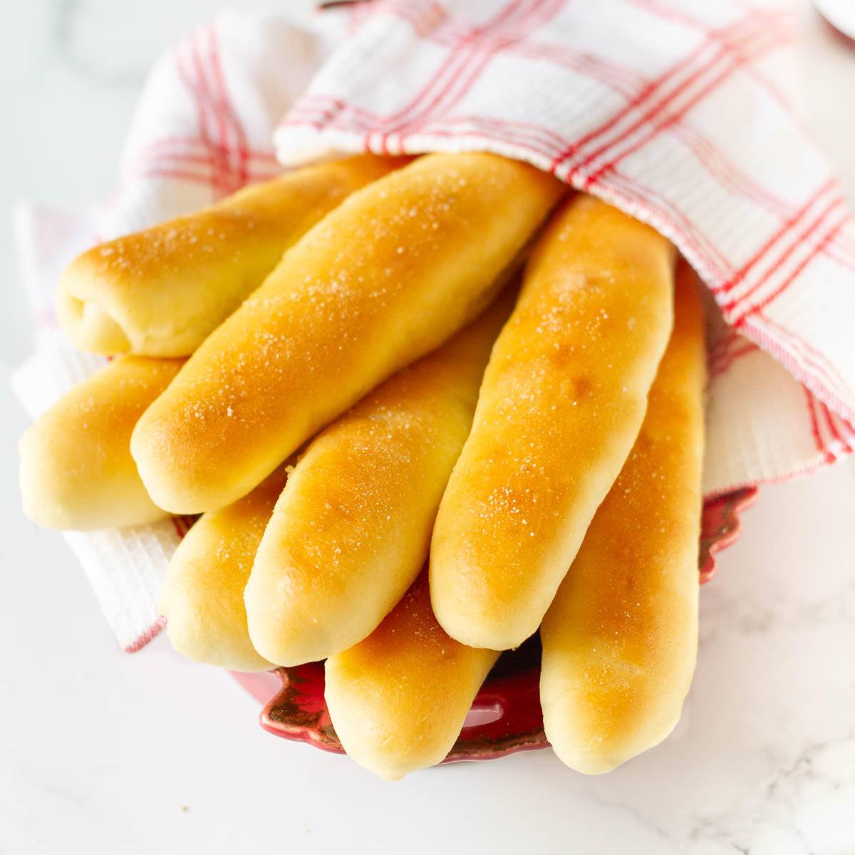 breadsticks wrapped in a kitchen towel in a bowl.