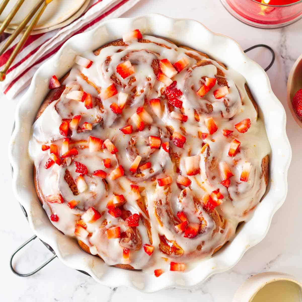 Strawberry rolls with glaze and fresh strawberries in a round baking dish.