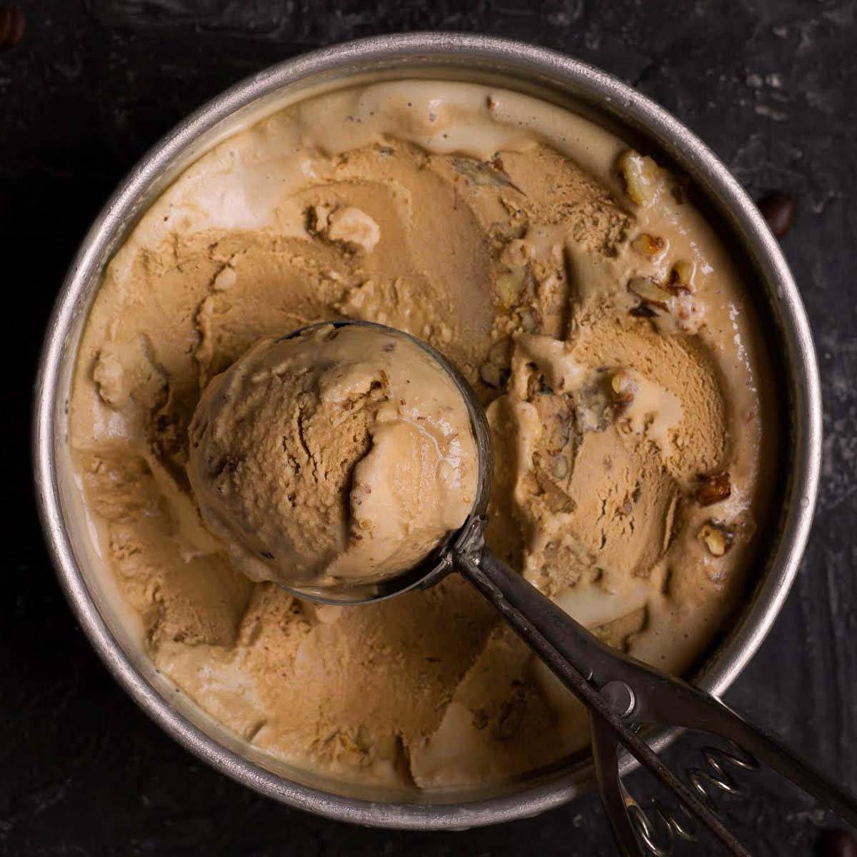 Coffee ice cream in a round dish with one scoop taken out with an ice cream scoop. 