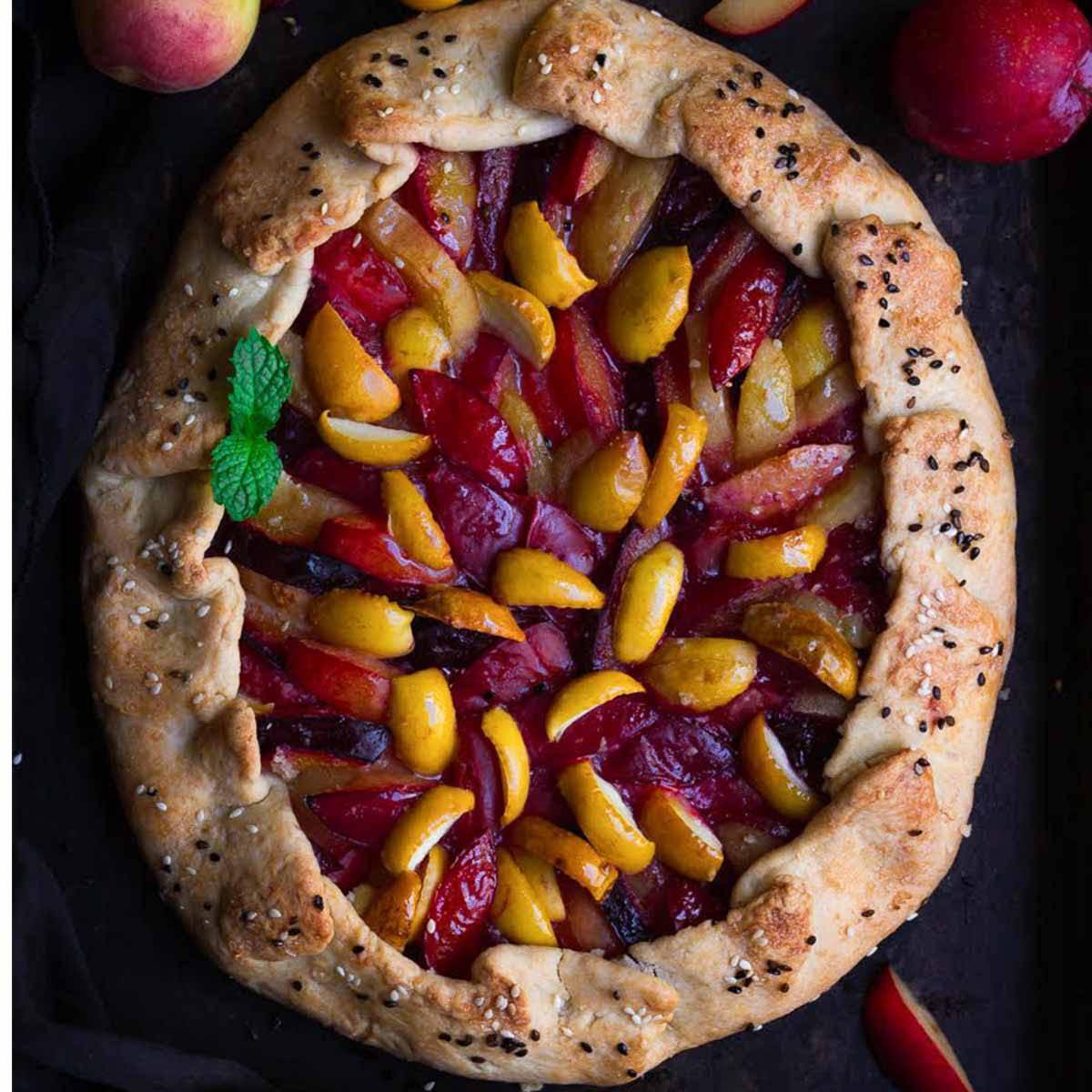 A galette with plums and apricots on a black tray