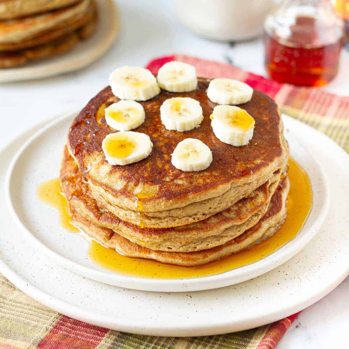 A stack of pancakes with with banana slices and maple syrup on top.