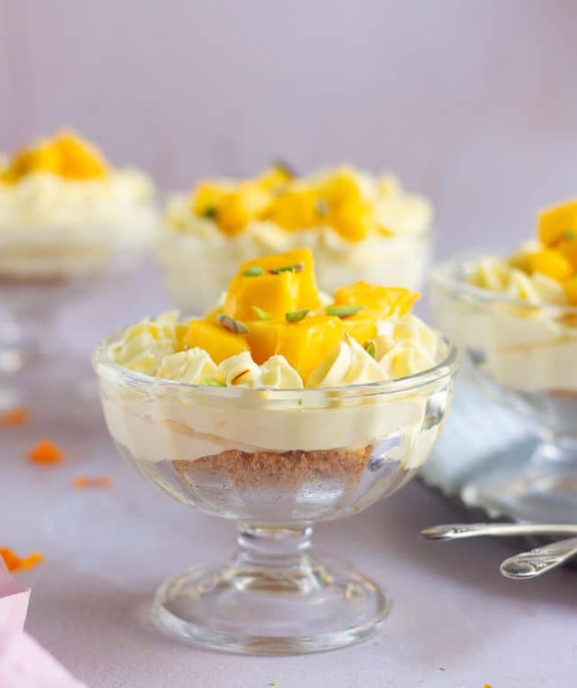 mango cheesecake in a dessert cup topped with mangoes and pistachios.