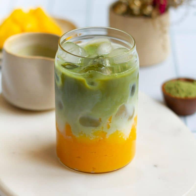 Mango matcha latte in a glass with ingredients around.