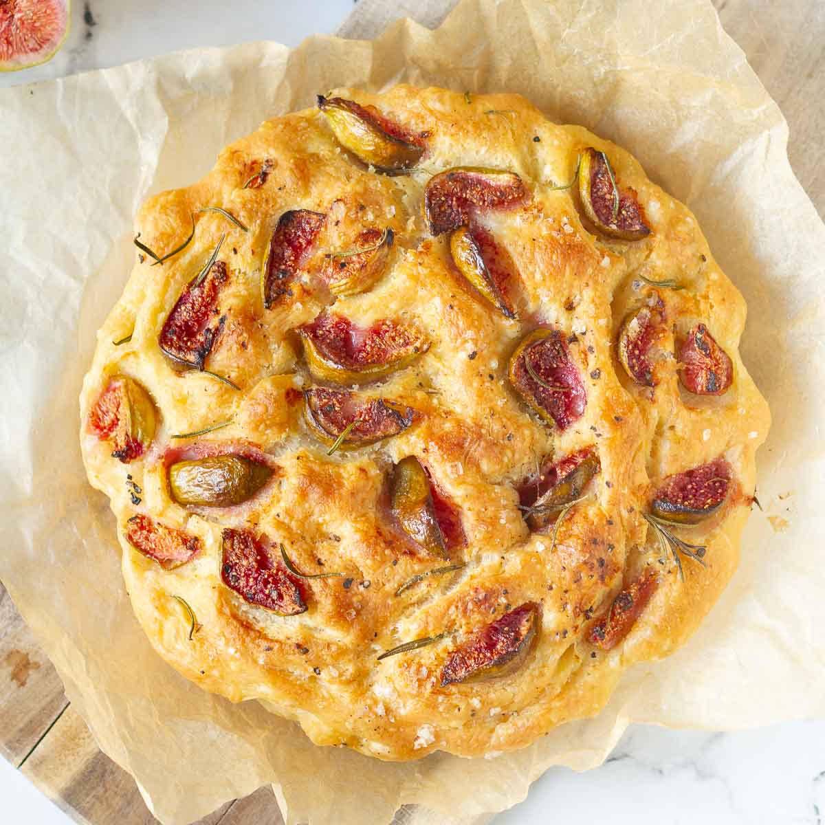 A focaccia with figs and rosemary on parchment paper.