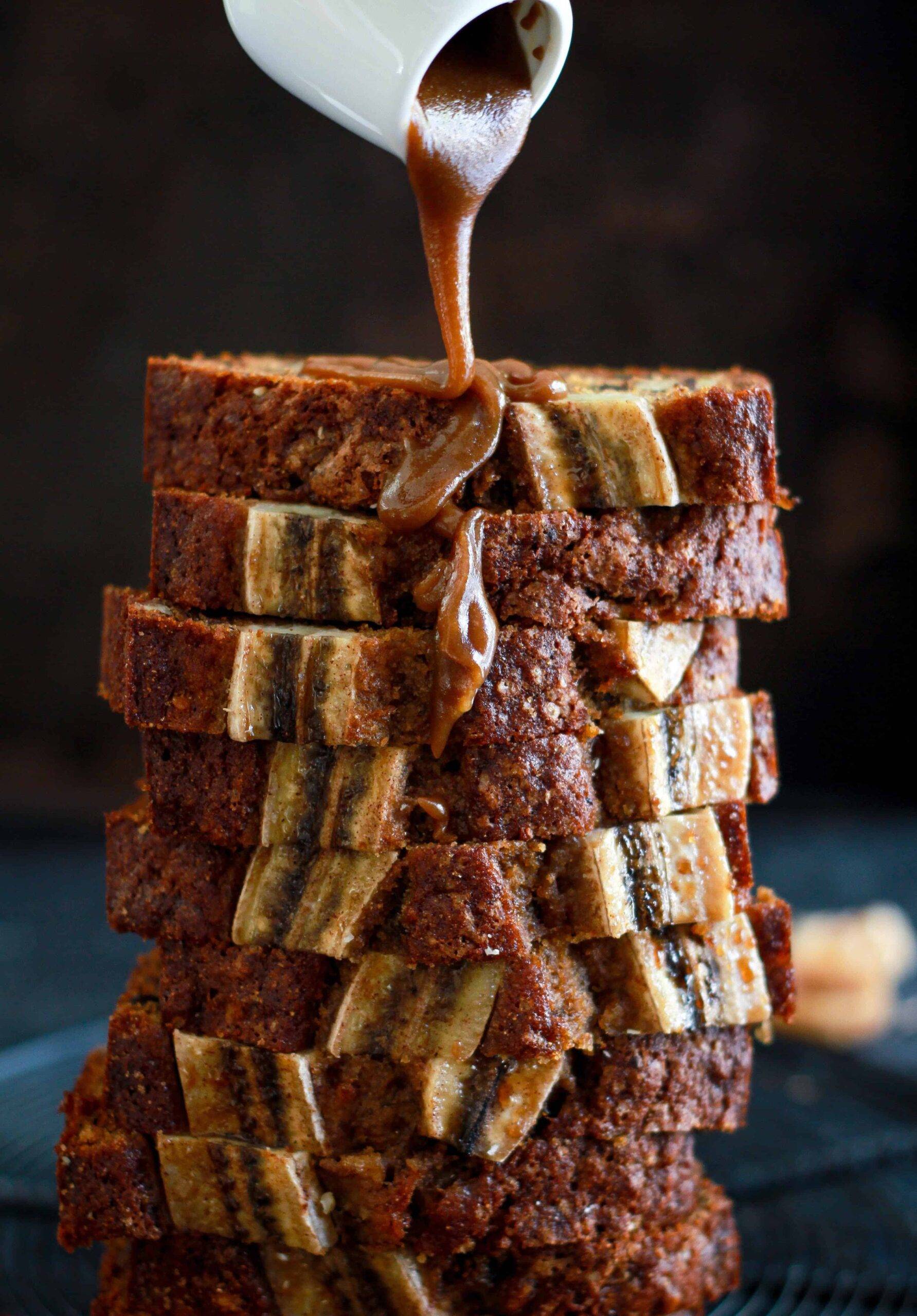 Slices of walnut fig banana bread stacked and caramel sauce being poured on top.