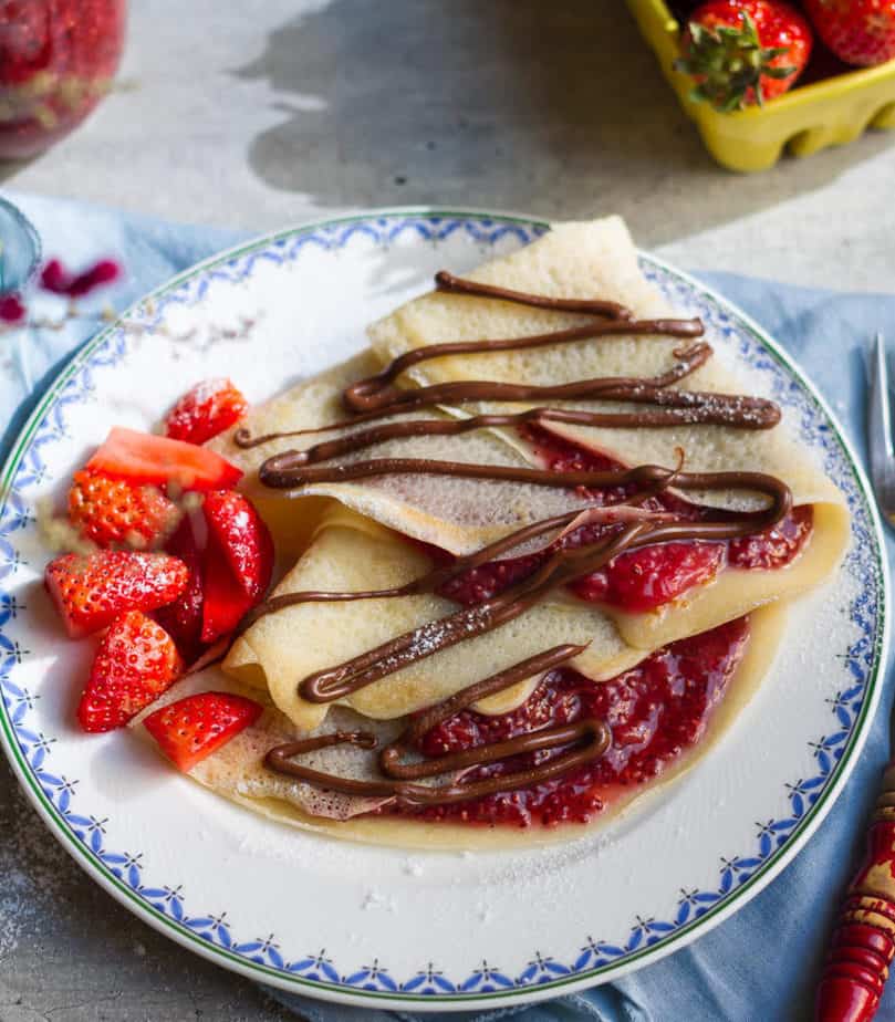 2 crepes filled with strawberry jam on a plate.