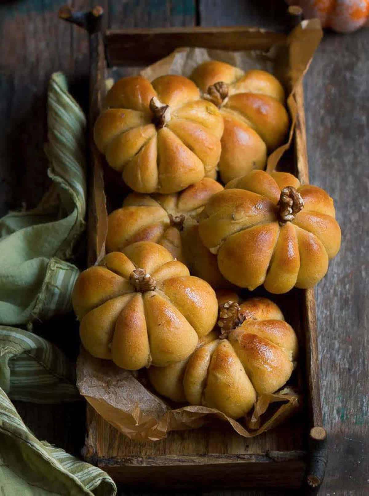 Pumpkin shaped bread rolls in a wooden tray.
