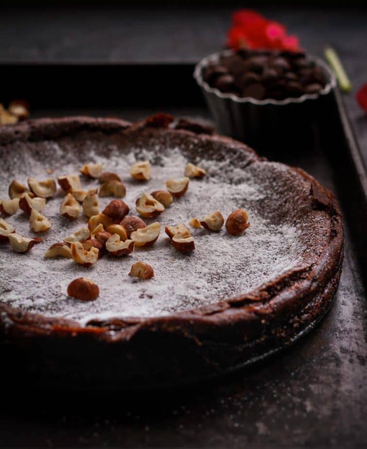 chocolate cake with hazelnuts on top on a black tray.