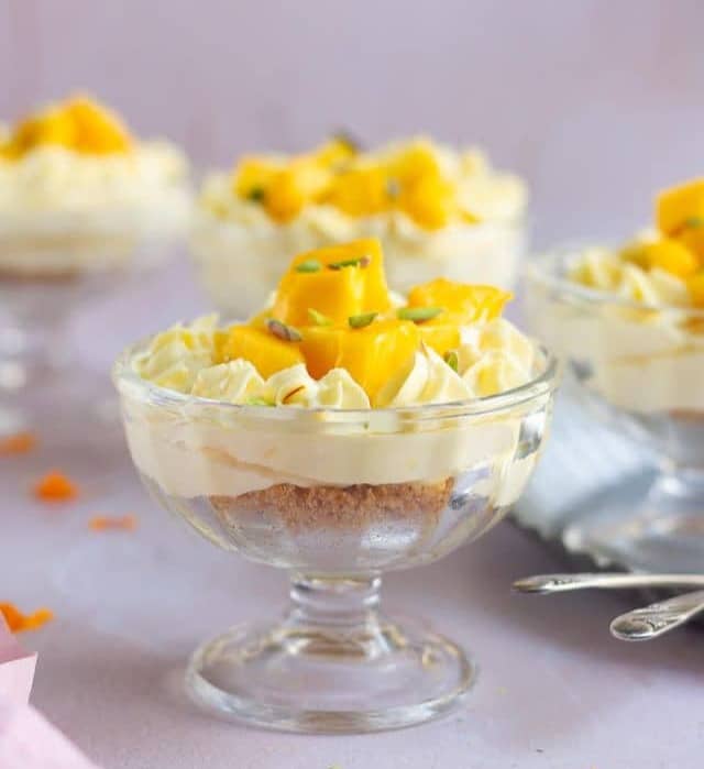mango cheesecake in a dessert cup garnished with mangoes and pistachios.