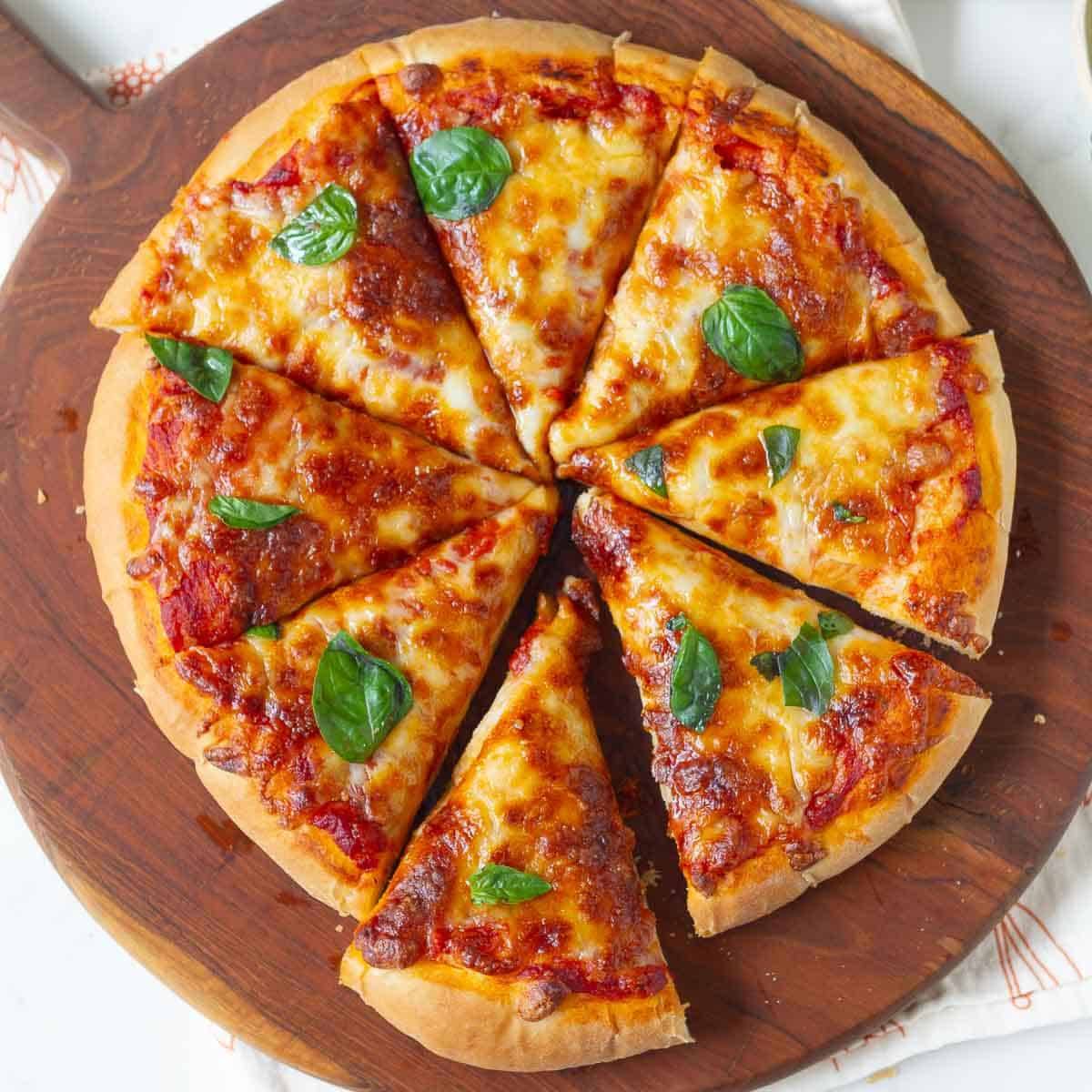 Sliced cheese pizza topped with basil on a wooden board.