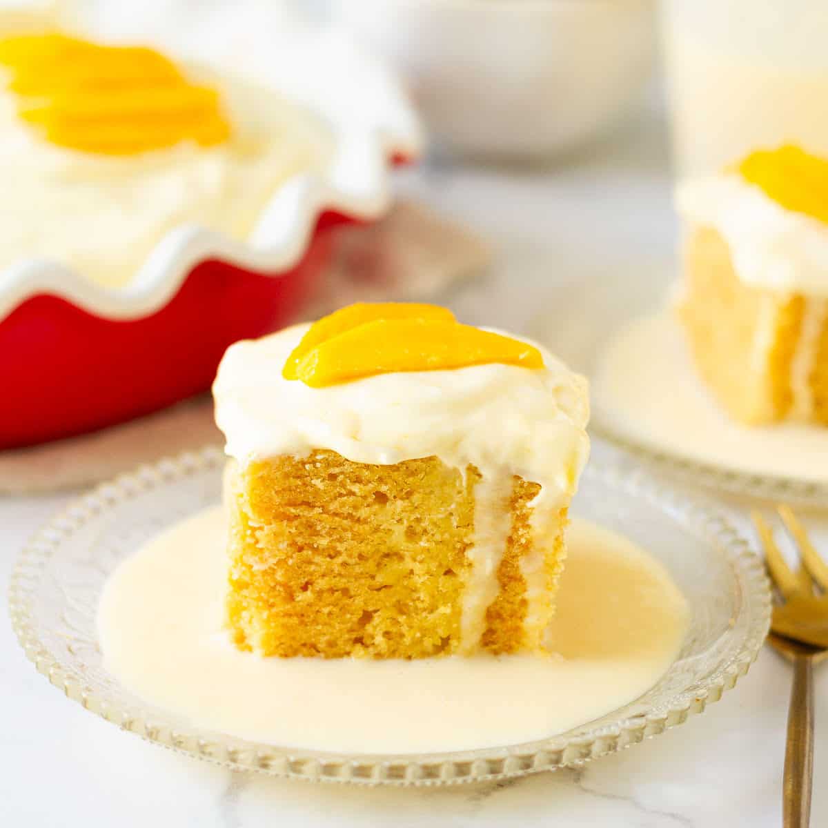 A slice of mango tres leches cake on a small plate with a fork on the side.
