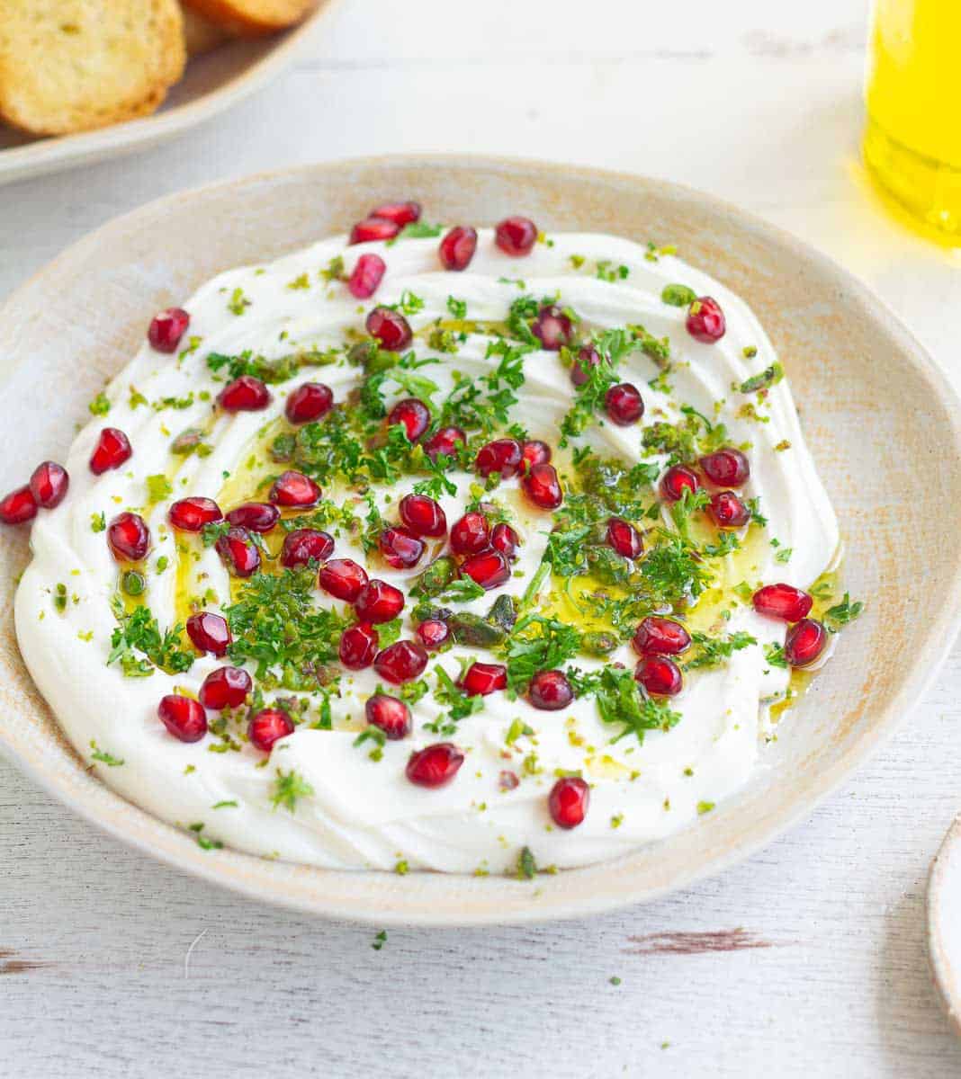 Creamy goat cheese dip topped with pomegranate arils and parsley in a bowl.