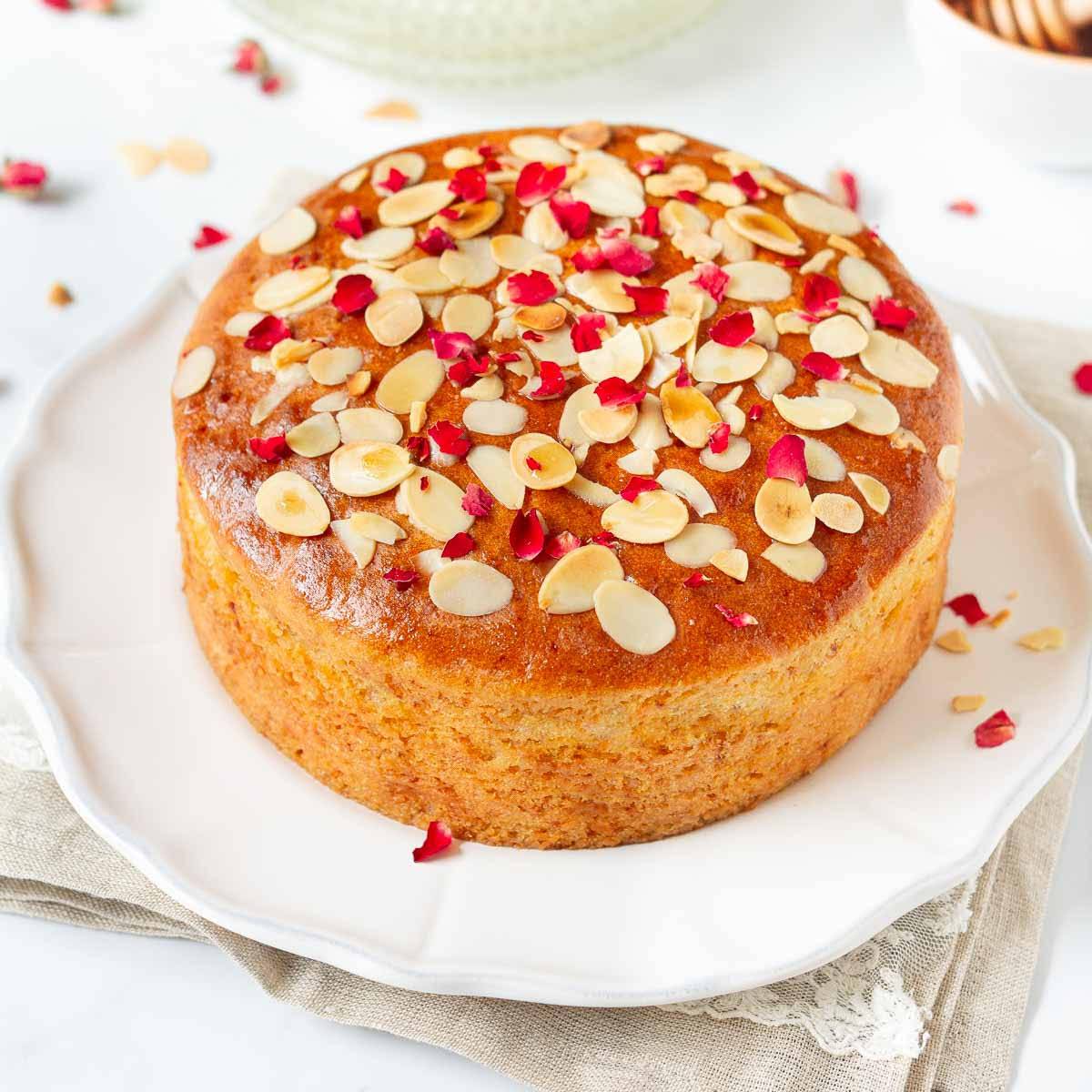 A cake with almonds and dried rose petals on a white platter.