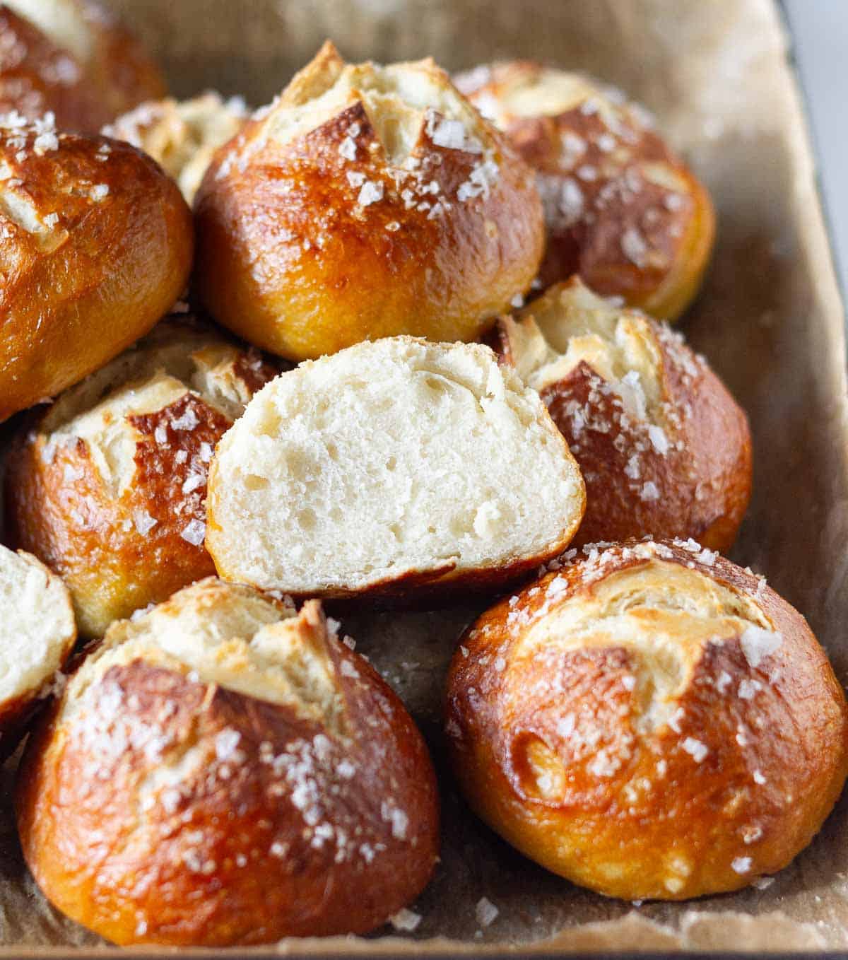 Half a pretzel bun on top of more buns in a baking tray.