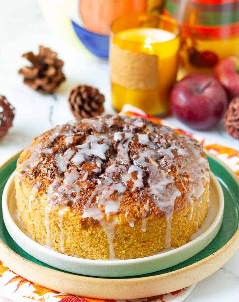 A cinnamon apple cake on a platter with a candle and apples in the background.