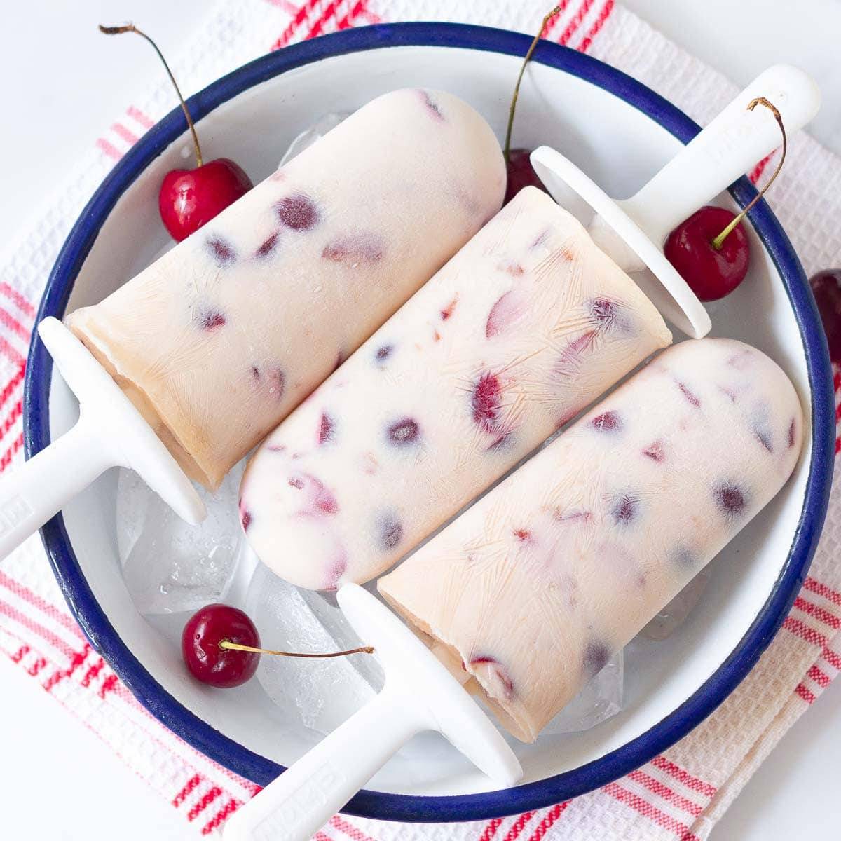 3 cherry popsicles in a white bowl.