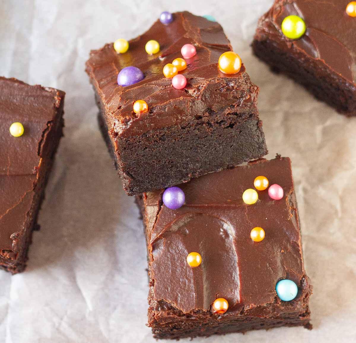 2 brownies topped with chocolate frosting and colourful sprinkles.
