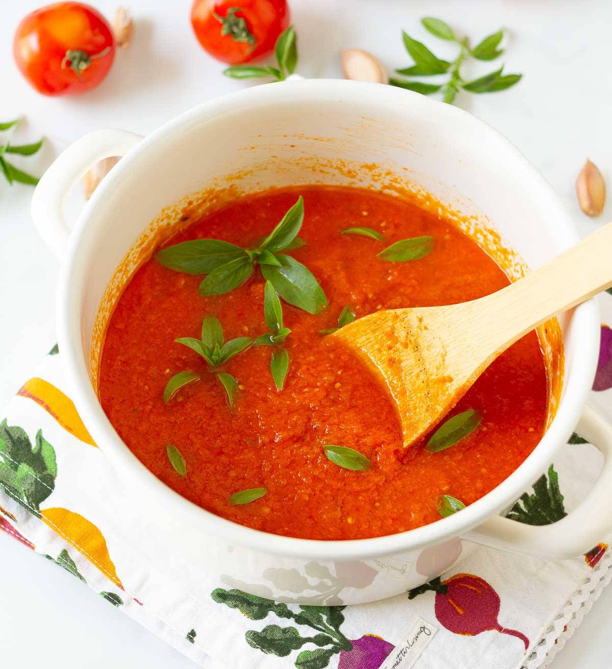 Tomato sauce with basil in a white pot with a wooden spoon.