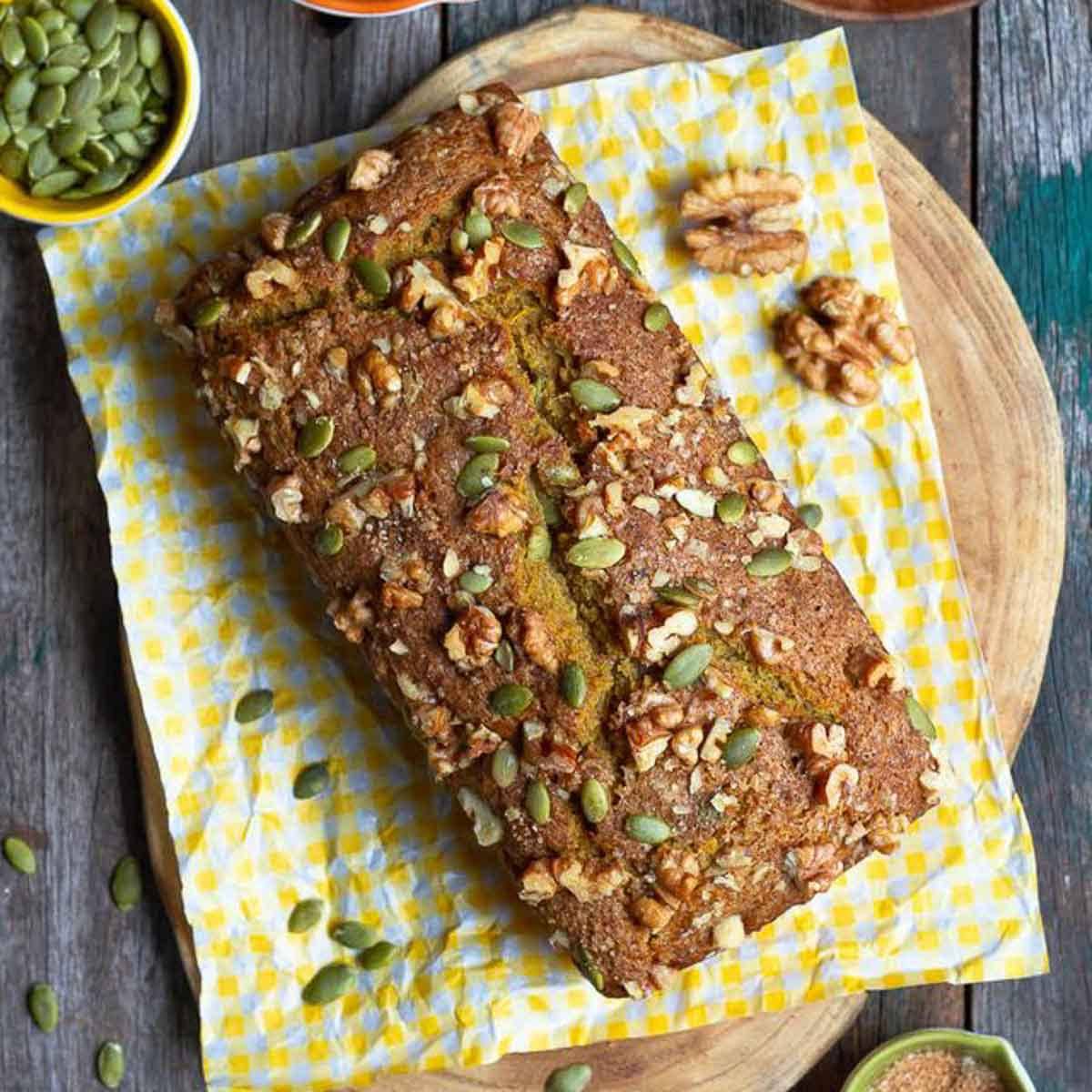 Pumpkin bread on a yellow tea towel on a wooden board.