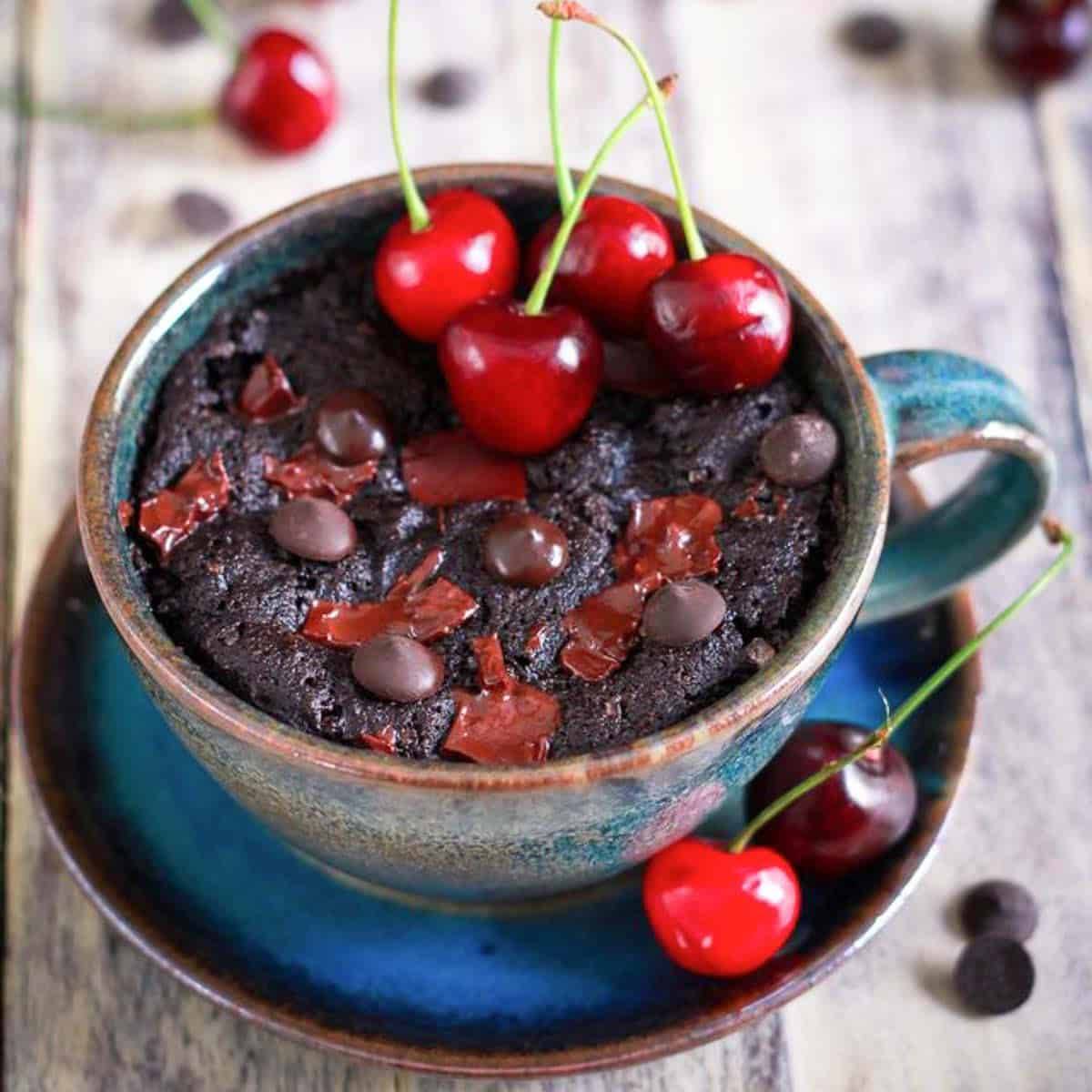 A chocolate mugcake with cherries in a blue cup.