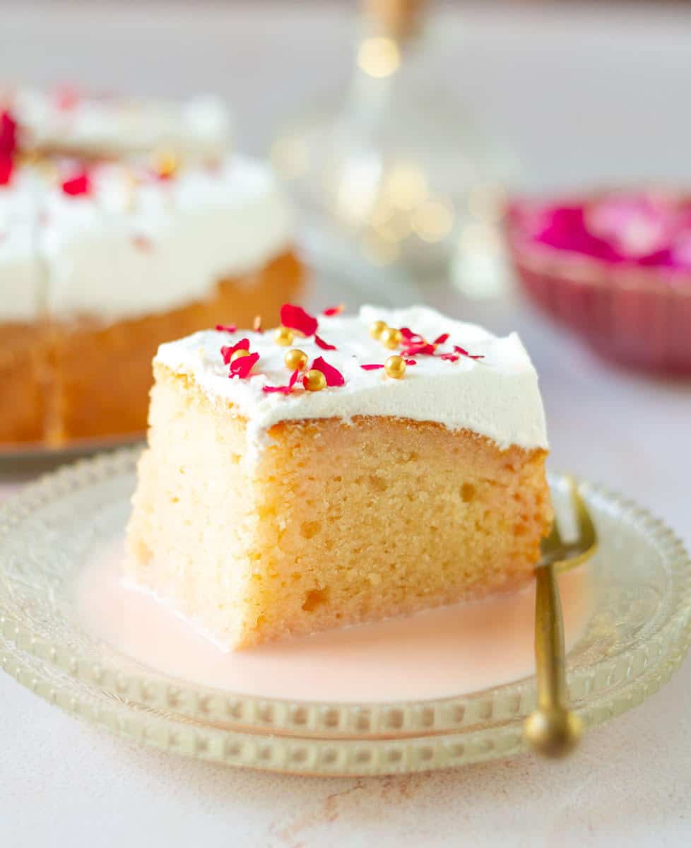 A slice of rose tres leches cake on a small plate with soaking syrup.