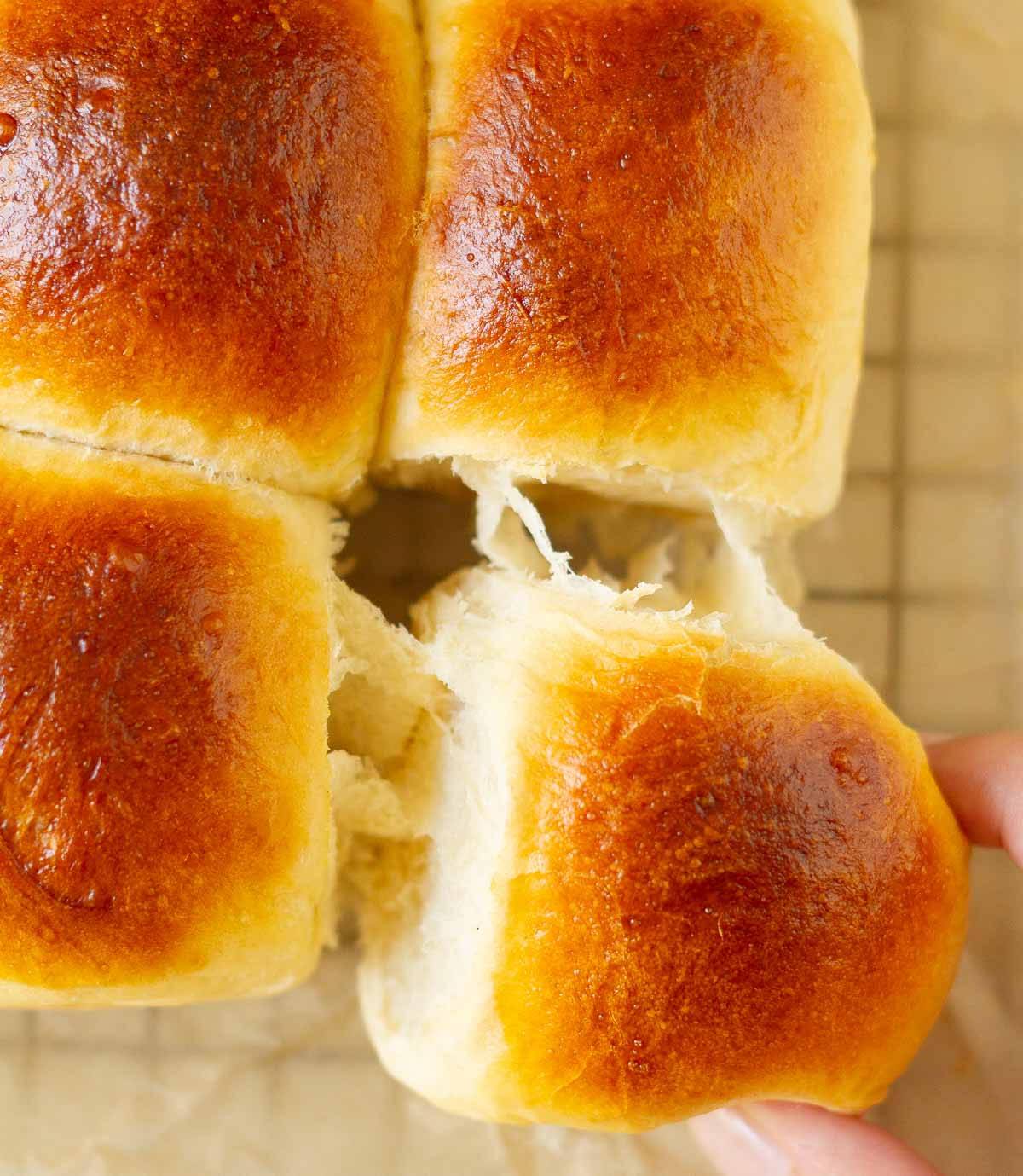 A hand pulling out a bread roll from a batch of bread rolls.