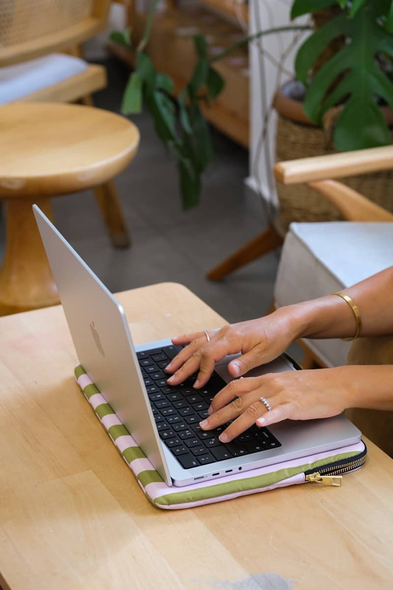 Hands typing on a laptop on a wooden table.