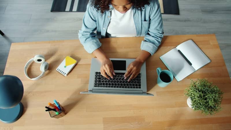 Woman typing on laptop at a wooden desk.