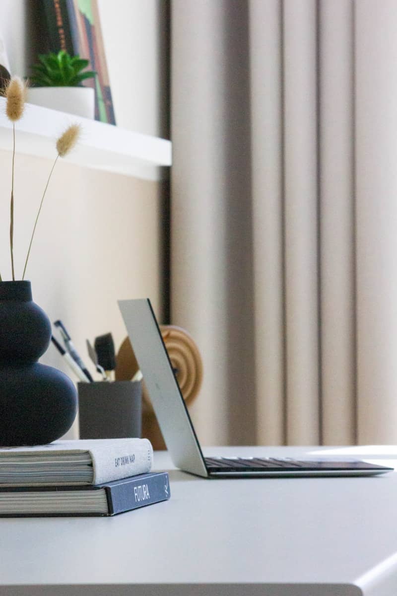 Desk with laptop, books, and vase.