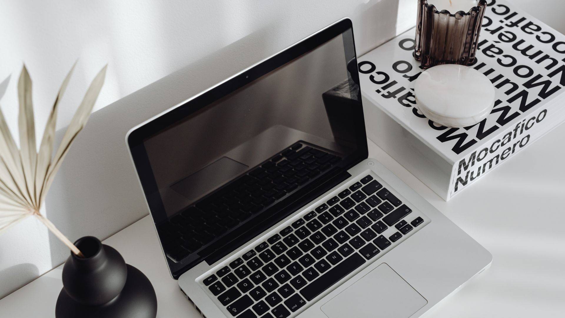 Decorative image only. Shows a laptop on a desk with a book next to it.
